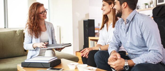 Real estate agent discussing strategy with a couple in a living room.