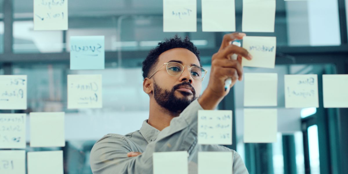Man writing on a clear board covered with sticky notes during a strategy planning session