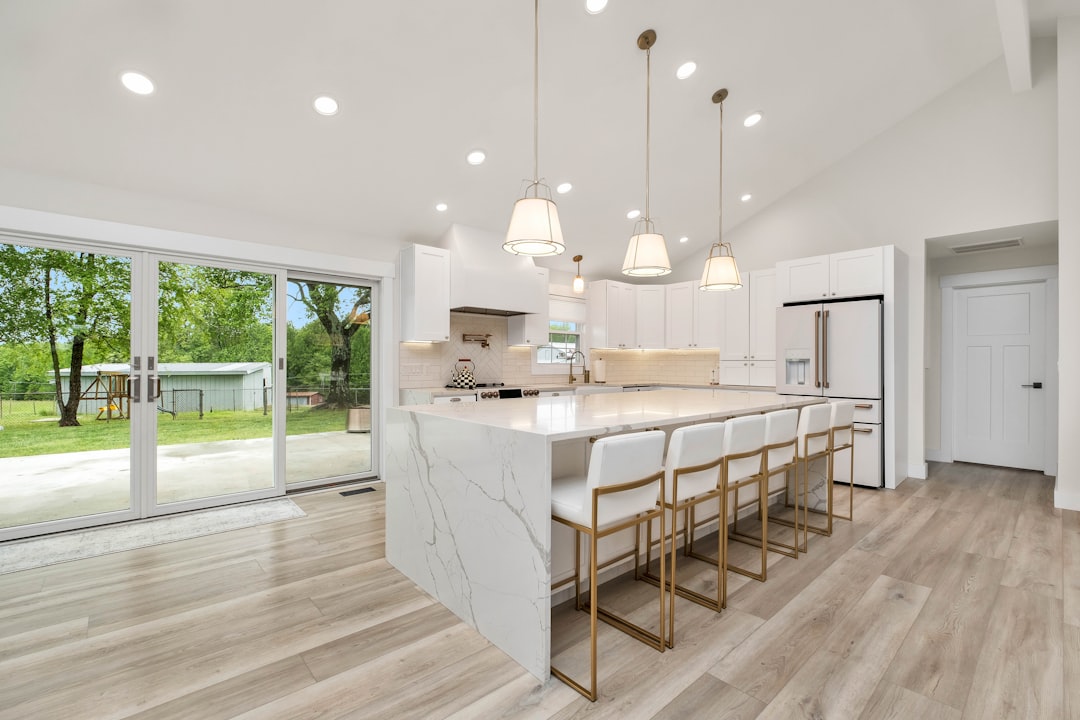 A homeowner sits at a modern kitchen island with a laptop and paperwork, researching low-commission real estate options for selling their home.